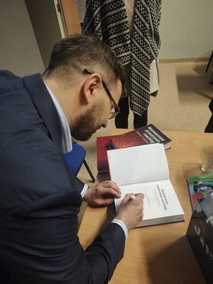 Zdjęcie Artura Włodarczyka podpisującego egzemplarz książki dla biblioteki